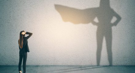 Thoughtful businesswoman with superhero shadow on concrete wall background. Confidence and success concept